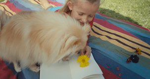 Little pretty girl looking notebook with herbarium. Sunny day, summer house. Interesting hobby. Funny dog playing with kid on lawn in garden. 4k raw slow motion footage video 60 fps