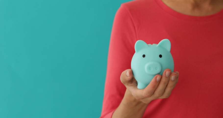 Positive female putting coin in piggybank, planning budget, financial savings on blue background