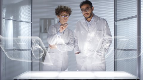 Male and female doctors in lab coats using futuristic computer with 3D hologram interface and discussing human heart projected in the air