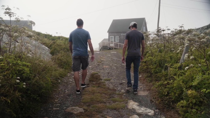 Two men seen from behind walking towards a small city fishing camp during a foggy day - slow motion.