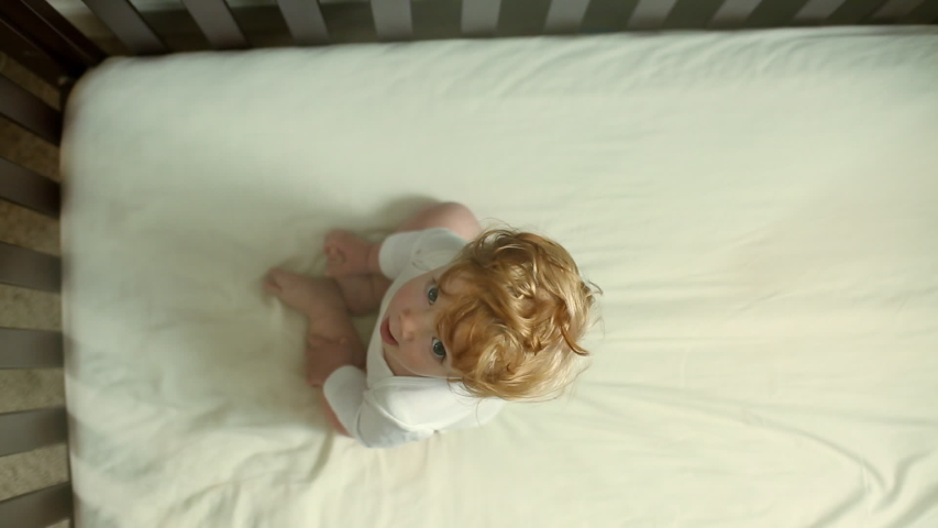 Directly above Caucasian baby boy with ruffled hair sitting in crib