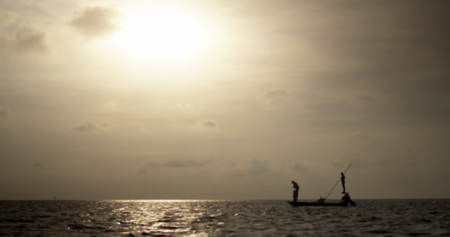 Silhouette of distant Caucasian men fly fishing on skiff boat