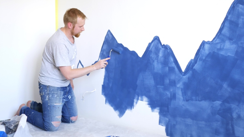 a man paints blue mountains on a bedroom wall