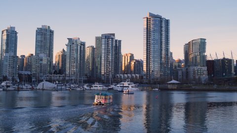 Vancouver , British Columbia / Canada - 03 17 2019: Vancouver, British Columbia, March 2019 - A WIDE SHOT of an Aquabus Driving Toward the Yaletown Dock Location with Vancouver's Downtown Sunset in th