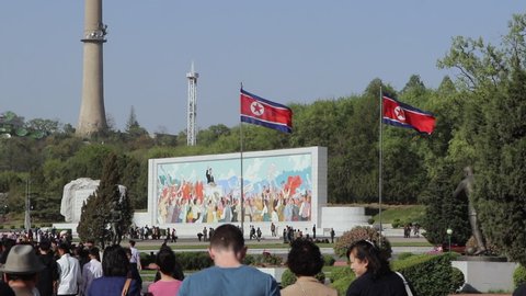 Pyongyang / North Korea - 05 16 2019: A crowded park with a painted wall monument surrounded by the North Korea flags in Pyongyang, North Korea.