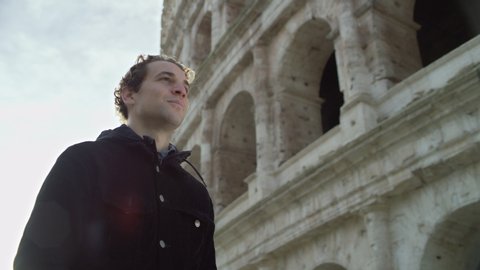 Happy, cheerful Italian man walking and looking up at the Coliseum, with soft natural light. Medium shot on 4k RED camera.