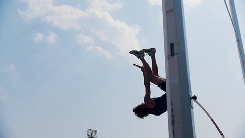 Pole vault training on the stadium outside- an athletic man jumping over the bar and falling down with the bar - unsuccessful attempt