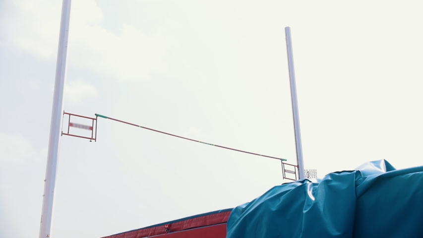 Pole vault training at stadium - a woman successfully jumping over the bar and falls on the mat