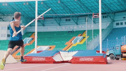 Pole vault training - an athletic man jumping over the bar in the stadium