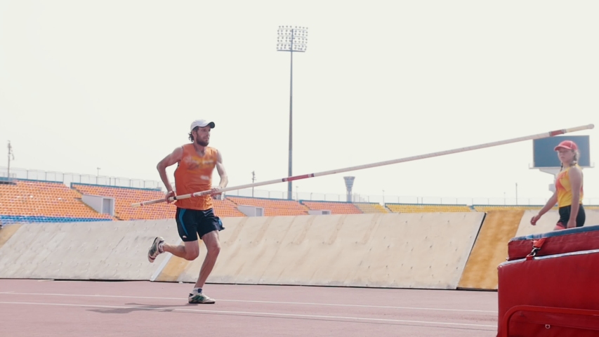 Pole vault training - a bearded athletic man jumping over the bar - a woman watching him