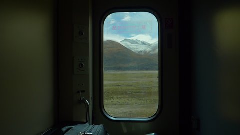 CLOSE UP: Breathtaking view of scenic landscape of Tibet through a small window in the luggage compartment of a sleeper train crossing China. Small window offers a view of snowy Himalaya and plains.
