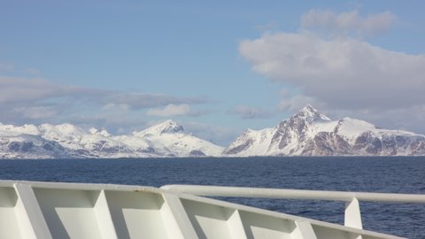 View from forward side of ship in the arctic outside Norway with snow covered mountains in the background.