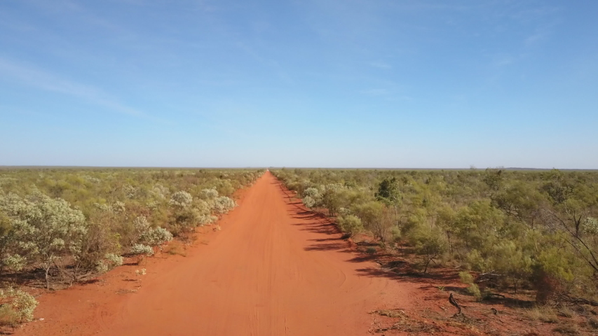 Panoramic aerial view of flight above straight red dirt track in outback Australia, with road, leading to horizon, green bush, sunny blue sky as background. | Shutterstock HD Video #1035254402