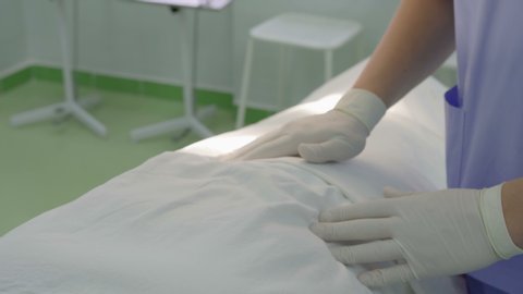 Close-up of the surgeon's hands in white protective rubber gloves, palpating the patient on the table in the operating room in the hospital. The concept of medicine and health
