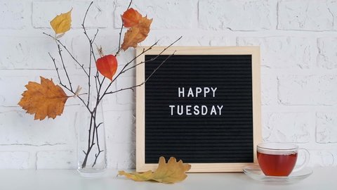 Happy Tuesday text on black letter board and bouquet of branches with yellow leaves on clothespins in vase on table Template for postcard, greeting card Concept Hello autumn Tuesday.
