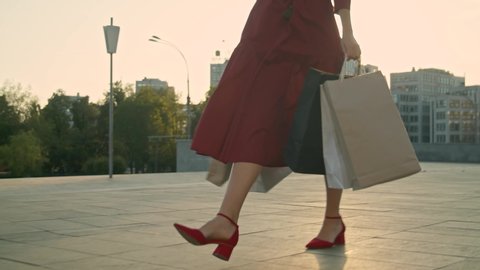 Young woman in red dress with shopping bags walks on the street during sunset