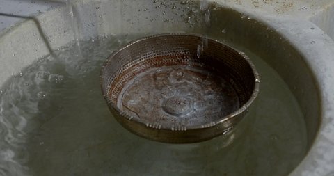 Close-up of slow motion water flows from the tap into the storage tank and an old Cup for watering the body in the Turkish bath Hammam