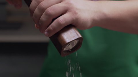Macro shot: chef uses salt mill to add some salt for his meal, salt falls in slow motion, milling the salt, using kitchen stuff, Full HD prores 422 HQ