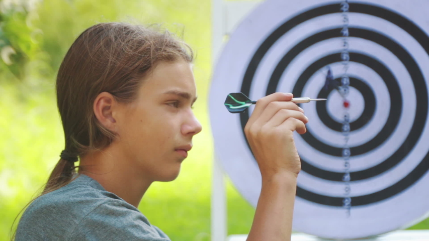 Portrait of a teenager boy playing darts. A boy plays an outdoor darts game.
