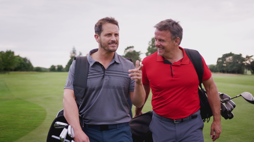 Two Mature Couples Playing Golf Walking Along Fairway Carrying Golf Bag