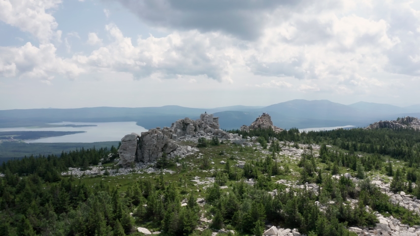 Aerial shot of a mountain range. At the top are marble cliffs. Unknown people on the rocks. Beautiful view from the mountain to the valley with the lake.