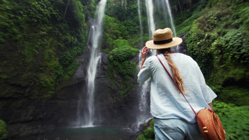Back of woman woman in straw hat enjoying breathtaking high waterfall Sekumpul in Bali rainforest. Great wild nature of Indonesia Royalty-Free Stock Footage #1035283574