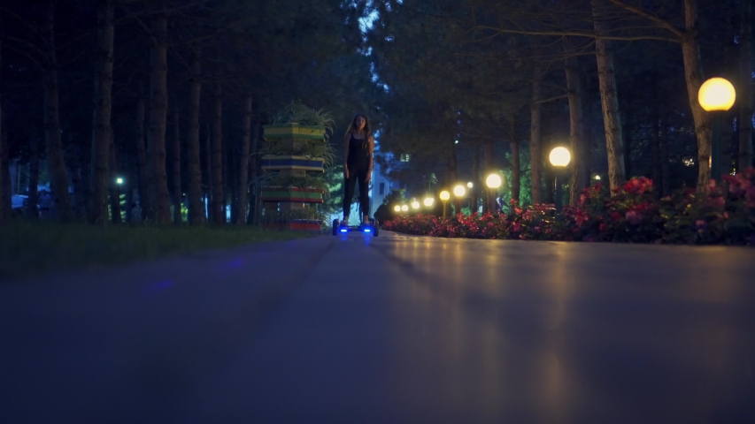 A girl riding a gyro scooter in the evening. Turned on lights in the evening park. Leisure