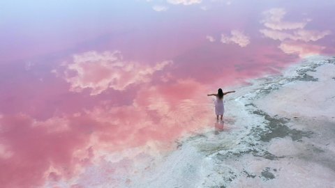 young woman walking and having fun near the unique lake with bright pink water color