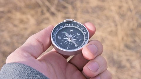 Close-up male hand holds a magnetic compass on a background of yellow dry grass in an outdor. The concept of reliable navigation in open areas and in the mountains