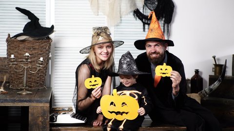 Happy family in costumes holds paper pumpkins on celebration of Halloween. Family has fun in Halloween time. Happy family. Halloween party and funny Pumpkin. Smiling family at halloween party