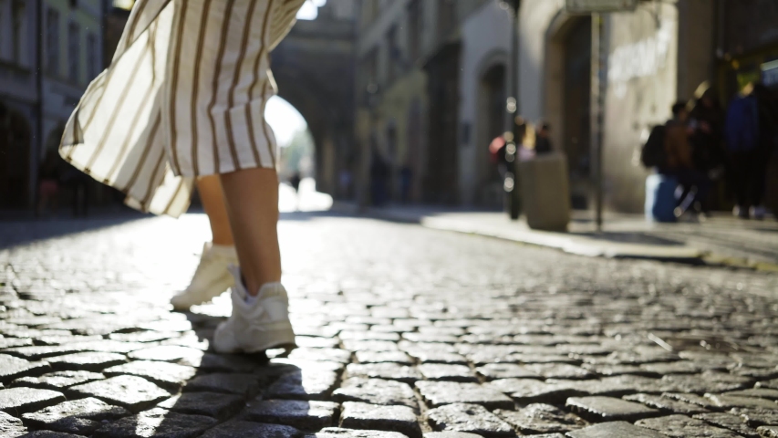 Following young woman tourist walking on the street of old town Prague at morning time. Low angle view legs moving on cobblestone pavement, girl enjoying sunny day, spinning and dancing in shining.