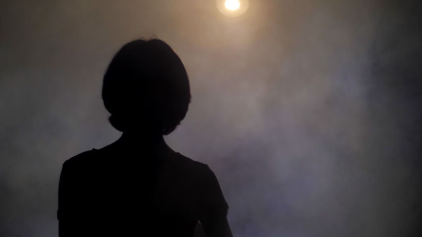 silhouette of young woman holding out hand to distant bright spotlight in fog backside view slow motion Royalty-Free Stock Footage #1035311081