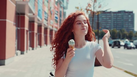 Adorable cute ginger curly Caucasian young woman enjoying her walk in the city on sunny day and eating delicious gelato ice-cream. Happiness, having fun, sweet tooth concept. Female portrait, close up