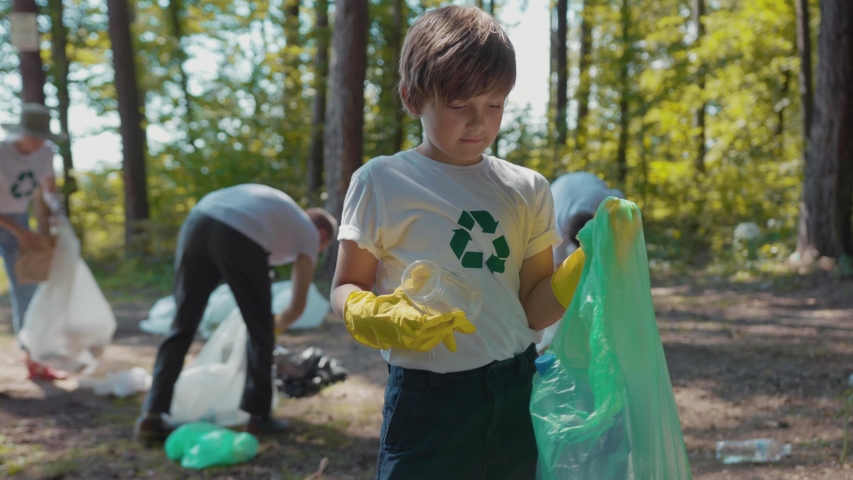 Happy boy voluteers activists child in gloves tidying up rubbish in park or forest look at camera smile  Royalty-Free Stock Footage #1035318245