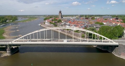 Decending 4k Aerial drone shot of the Wilhelmina bridge above the river the IJssel showing the sunny skyline of the old Dutch Hanza city Deventer and its landmark church tower of the Lebuinus kerk.