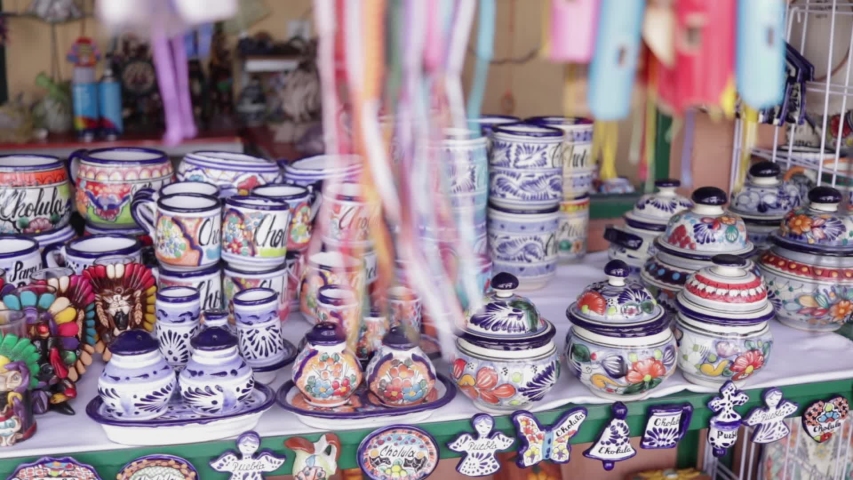 Slow panoramic view from right to left. Mexican Accessories market with ceramic plates and head skulls decorated in traditional Mexico style. Cholula, Puebla Mexico Royalty-Free Stock Footage #1035328787