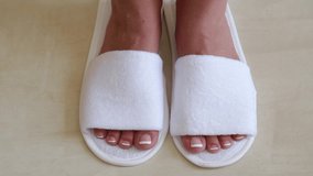 Closeup top view of female legs wearing white slippers. Happy woman standing in new slippers in hotel room. Real time full hd video footage.