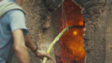 Yangon / Myanmar - 05 31 2019: Adult Burmese male using Bamboo stick to stoke the flames inside a limestone kiln in Myanmar