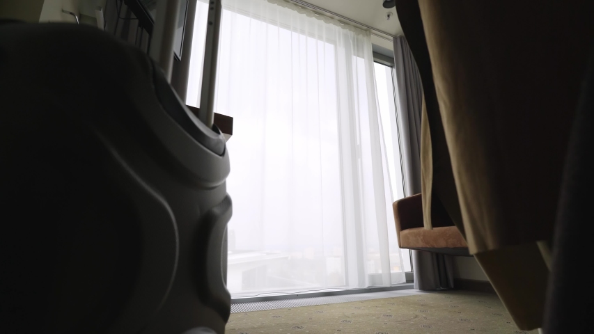 Back view silhouette woman just arrived in hotel apartment. low angle view girl coming to full length window, opening curtains, throwing hat and stretched out arms enjoying view.