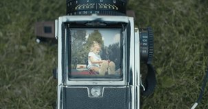 Shooting little girl's portrait with old medium format camera. Cute kid blowing a soap bubbles in garden. Sunny day. 4k raw slow motion footage video 60 fps