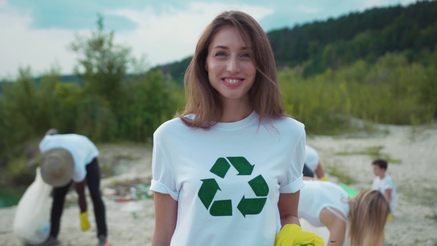 Pretty caucasian girl picking up garbage at sandy beach. Portrait of smiling female eco fighter helping environment cleaning nature from pollution. | Shutterstock HD Video #1035365387