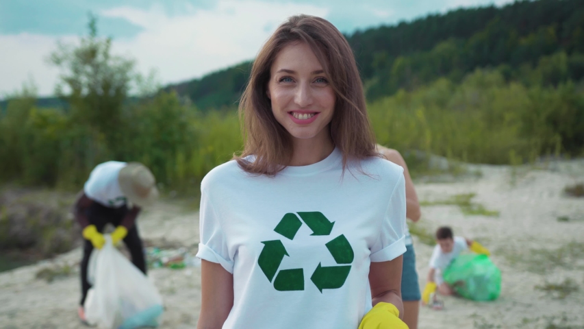 Beautiful portrait of smiling girl having good time cleaning up the beach from litter with friendly eco team. Charity cleaning up operation. | Shutterstock HD Video #1035365390