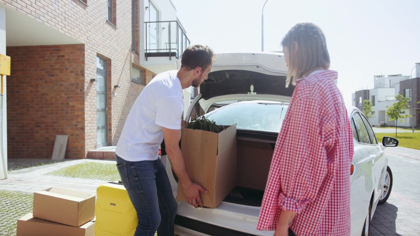 Beautiful family get out from the car and unload boxes to the new house adults moving to a new apartment in a lovely area on a sunny day baggage arrive siblings close up slow motion Royalty-Free Stock Footage #1035366011