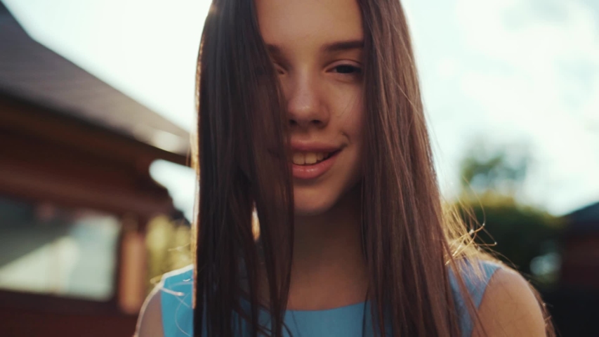 Beautiful attractive girl looking at camera and smiling hair fluttering in wind in the sun at sunset relaxing outdoors park summer teenage cute face female attractive field freedom slow motion