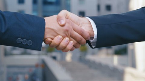 Close up of the hands of top managers in business suits, shake hands with each other, at Business center background, agree to a deal or say hello. Slow motion, unrecognizable person