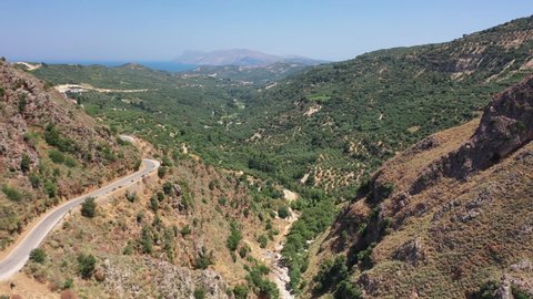 Aerial bird's-eye view video from drone of flight from Topolia Gorge canyon to a mountain valley with olive groves and mountain Topolia village. Kissamos, Chania prefecture, Crete, Greece.