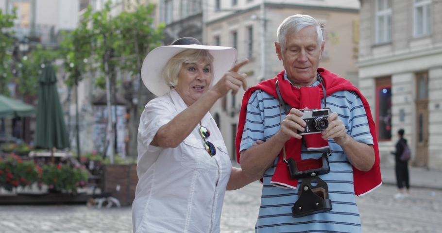 Senior two male and female tourists standing in town center while traveling in Lviv, Ukraine. Elegant woman in hat. A man with photo camera makes a photo. Vacation concept