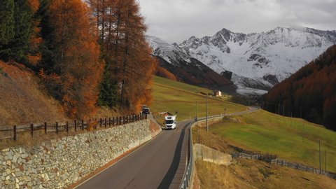 Slow Motion Aerial Pan: White RV Drives Past Stunning View of Langtauferer Mountains, Autumnal Trees and Green Fields - South Tyrol, Italy