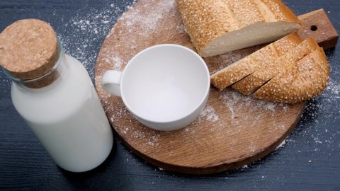Close up of pouring milk in white cup in a wooden background next to bread.