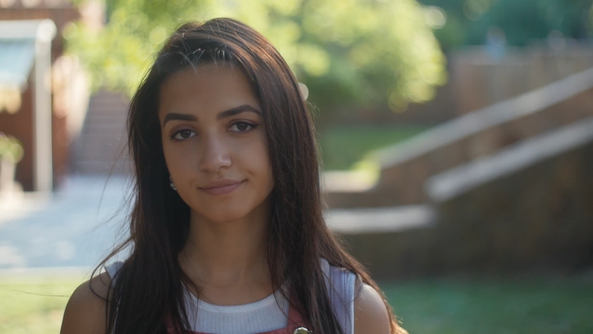 Portrait of amazing cute young girl with brunette hair looking at camera in the park, Slow motion